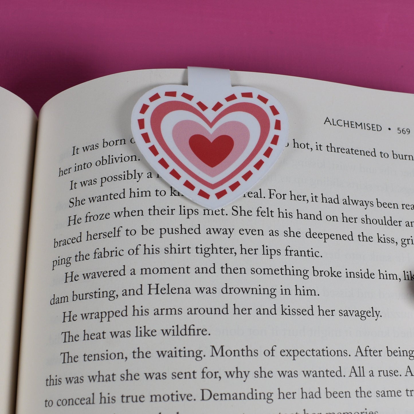 Open book with a heart-shaped sticker on a pink background