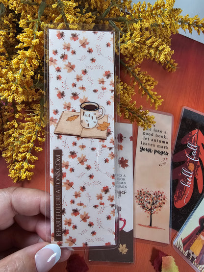 Hand holding a decorative box with autumn leaf pattern on a wooden surface with other items.