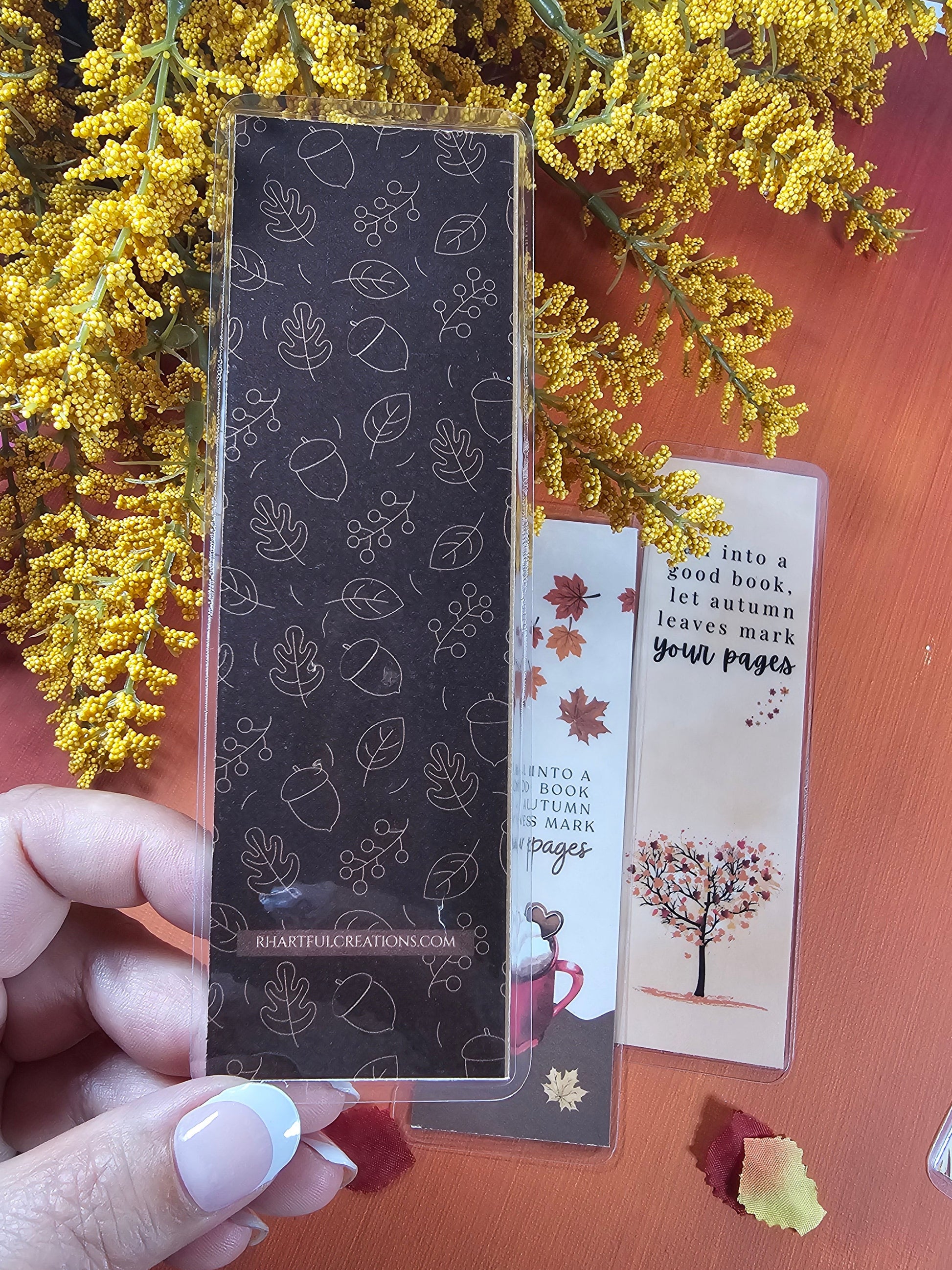 Hand holding a black rectangular product with floral patterns on a wooden surface with yellow flowers.