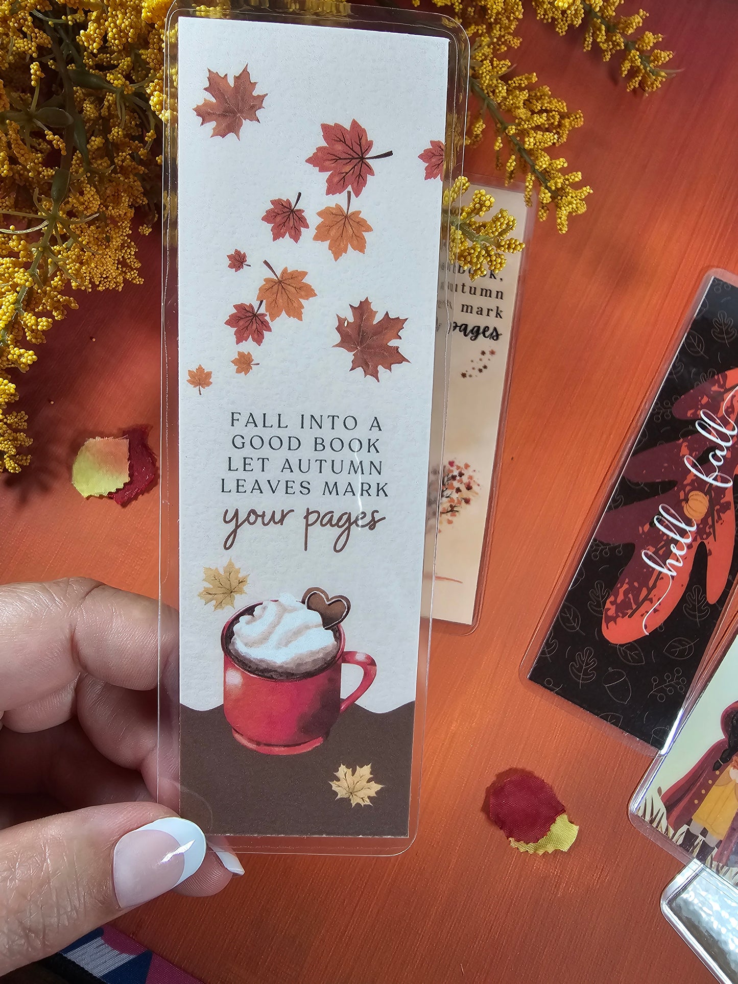 Bookmark with autumn leaves and a mug design on a wooden surface.