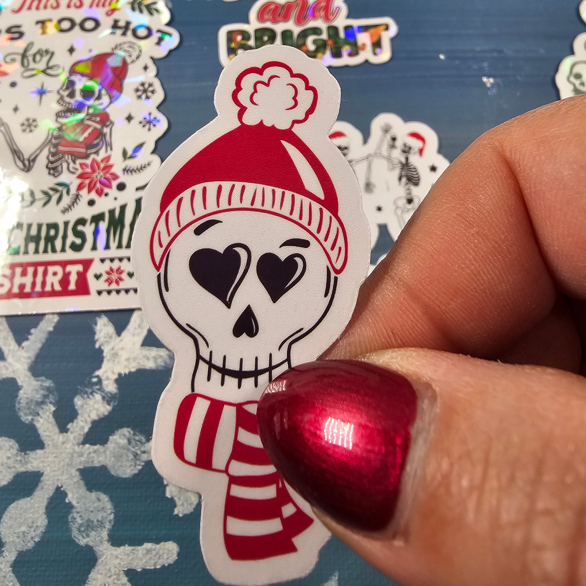 Hand holding a Christmas-themed sticker with a snowman design on a blue background with snowflakes.