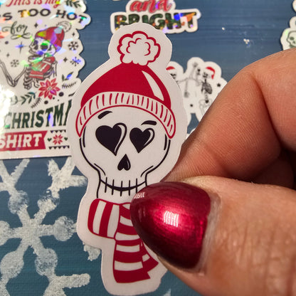 Hand holding a Christmas-themed sticker with a snowman design on a blue background with snowflakes.