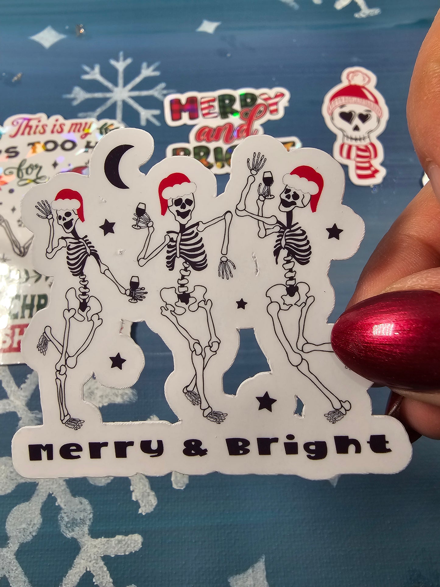 Decorative paper cutout with skeletons and 'Merry & Bright' text on a blue background.