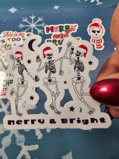 Decorative paper cutout with skeletons and 'Merry & Bright' text on a blue background.