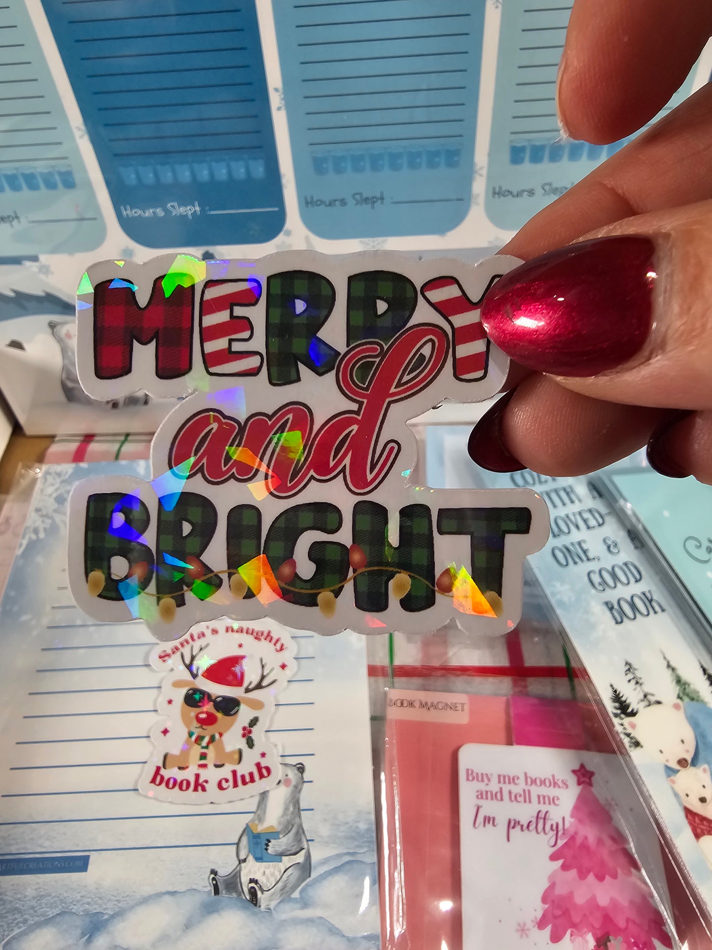 Hand holding a 'Merry and Bright' Christmas-themed card with colorful lights on a bookshelf background.