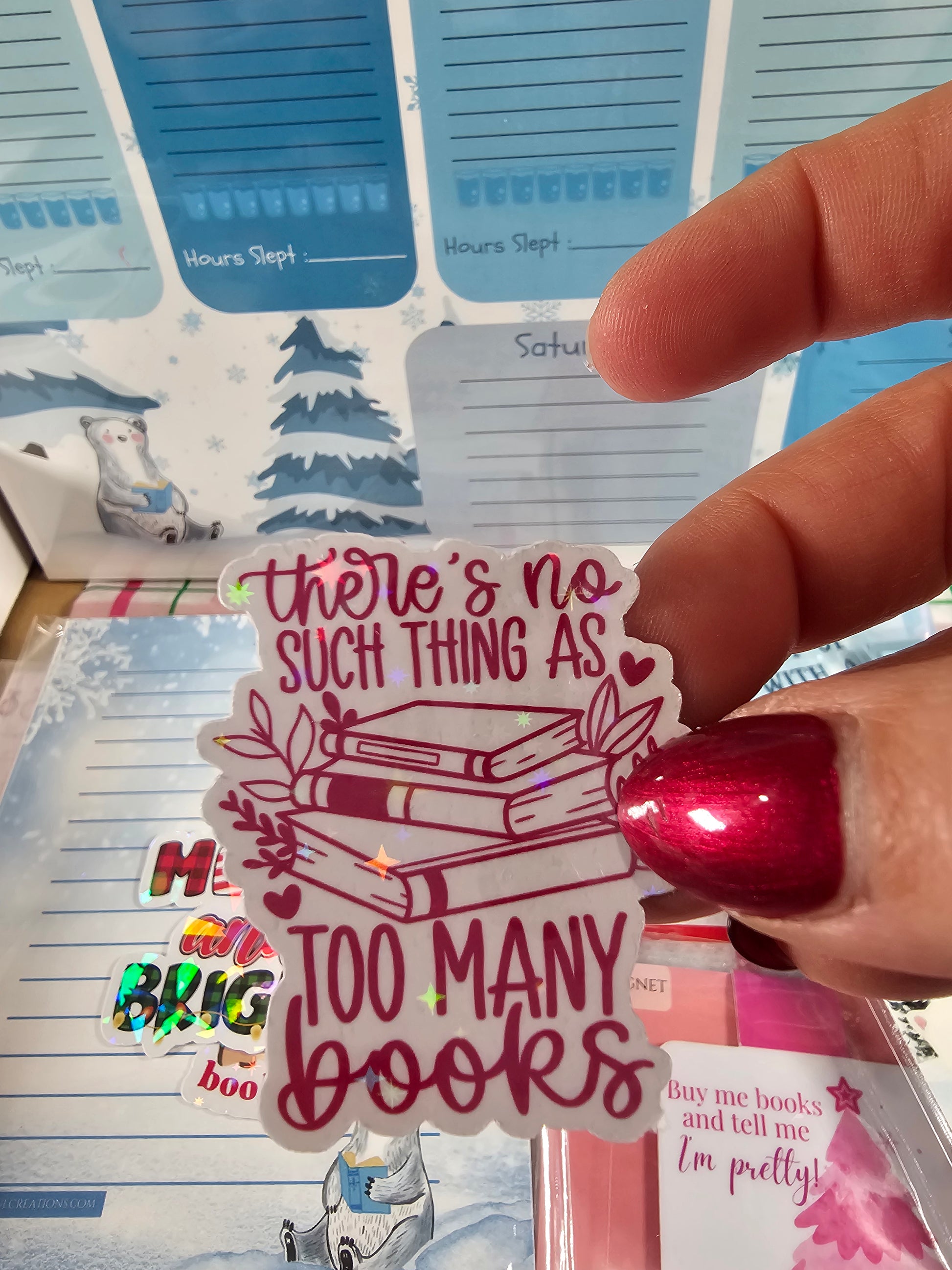 Hand holding a sticker with text and book illustrations over a background of colorful bookmarks.