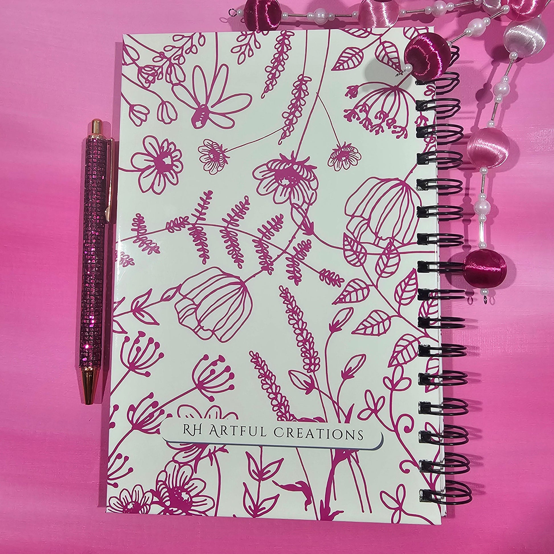 Notebook with floral design and pen on a pink background