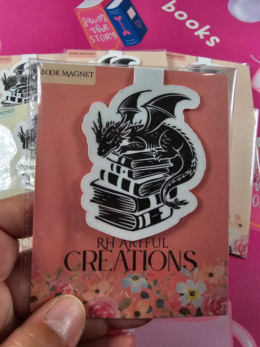 Book magnet with dragon design on a book, held against a pink background with 'books' text.