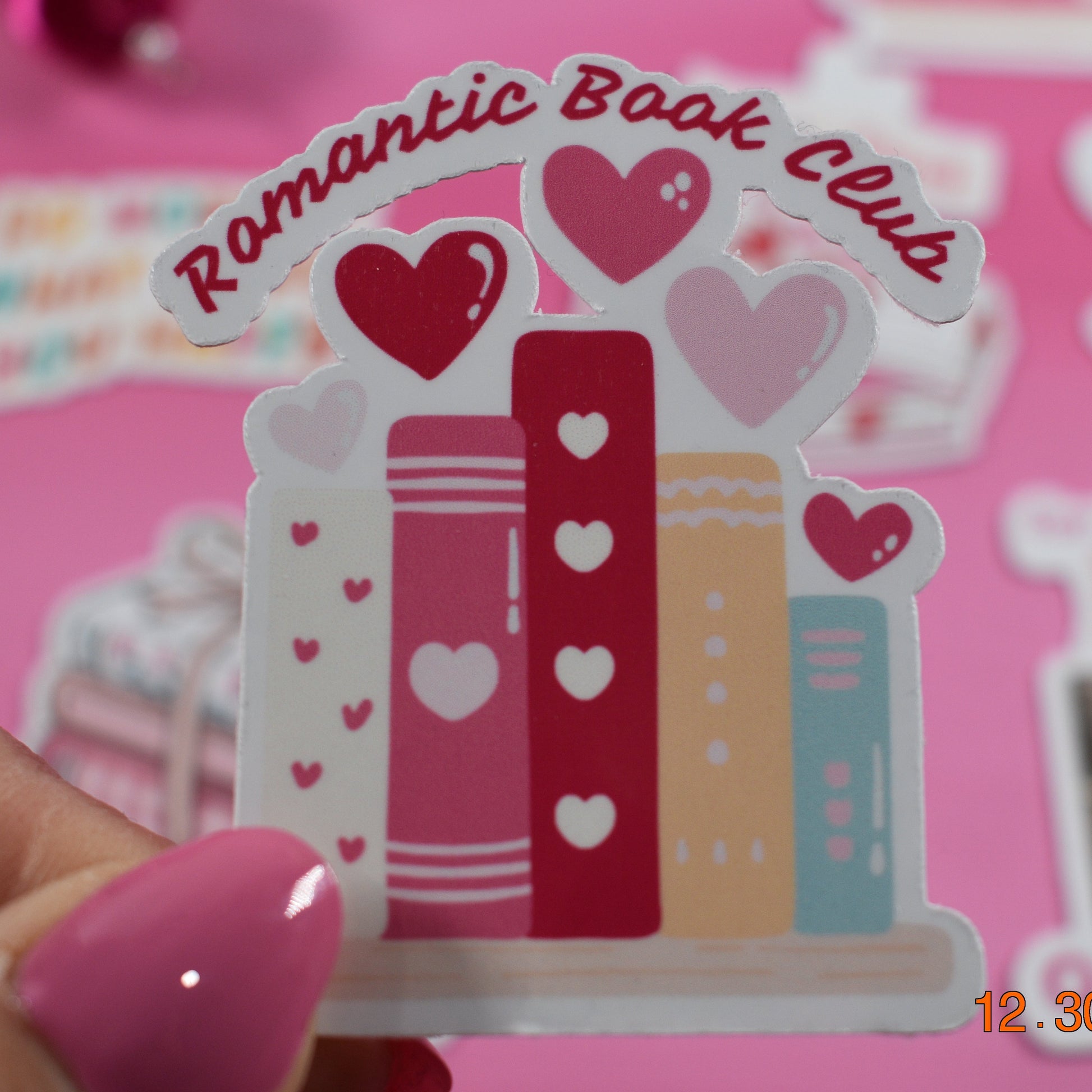 Sticker with 'Romantic Book Club' design held by a hand on a pink background