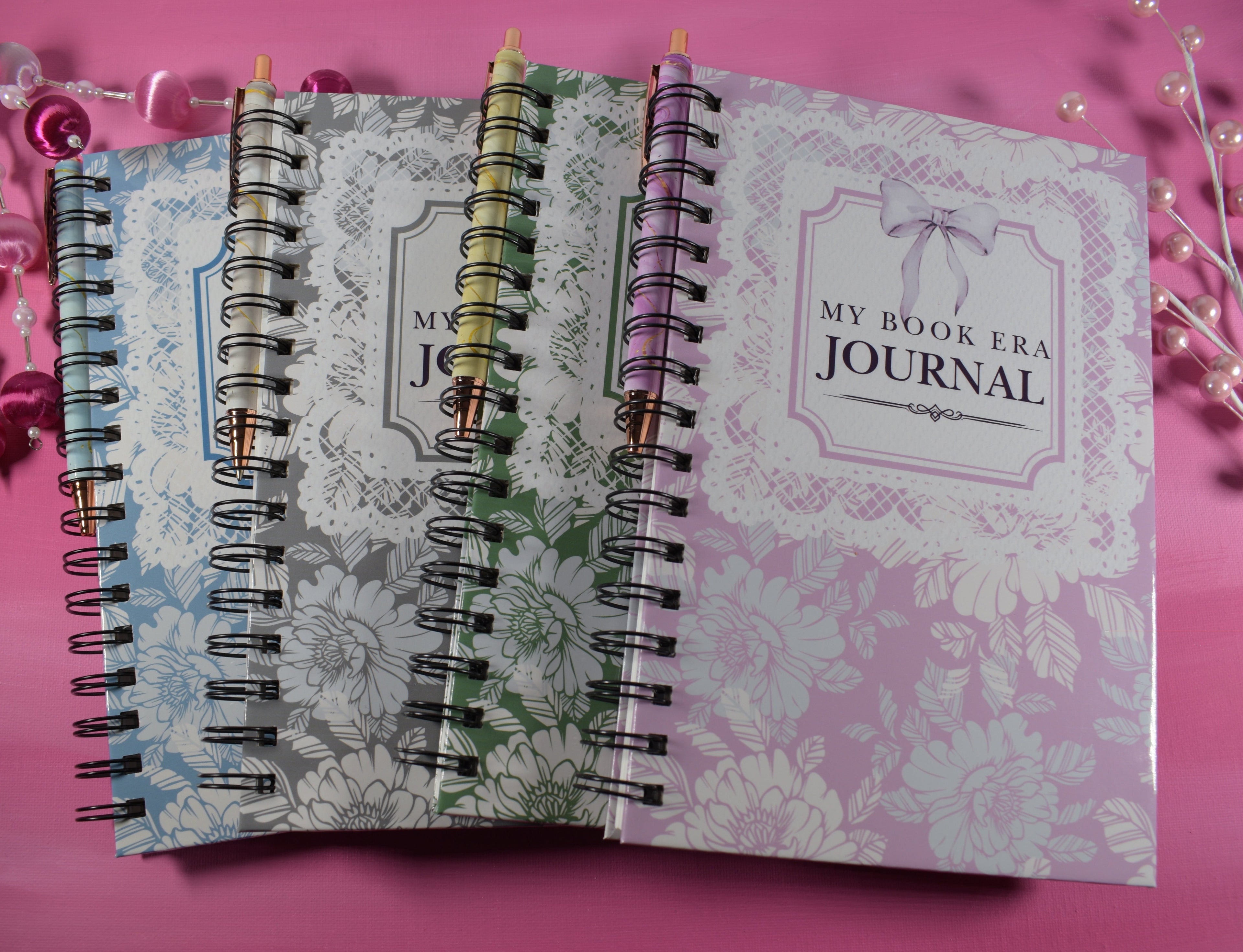 Two spiral-bound journals on a pink background with decorative items.