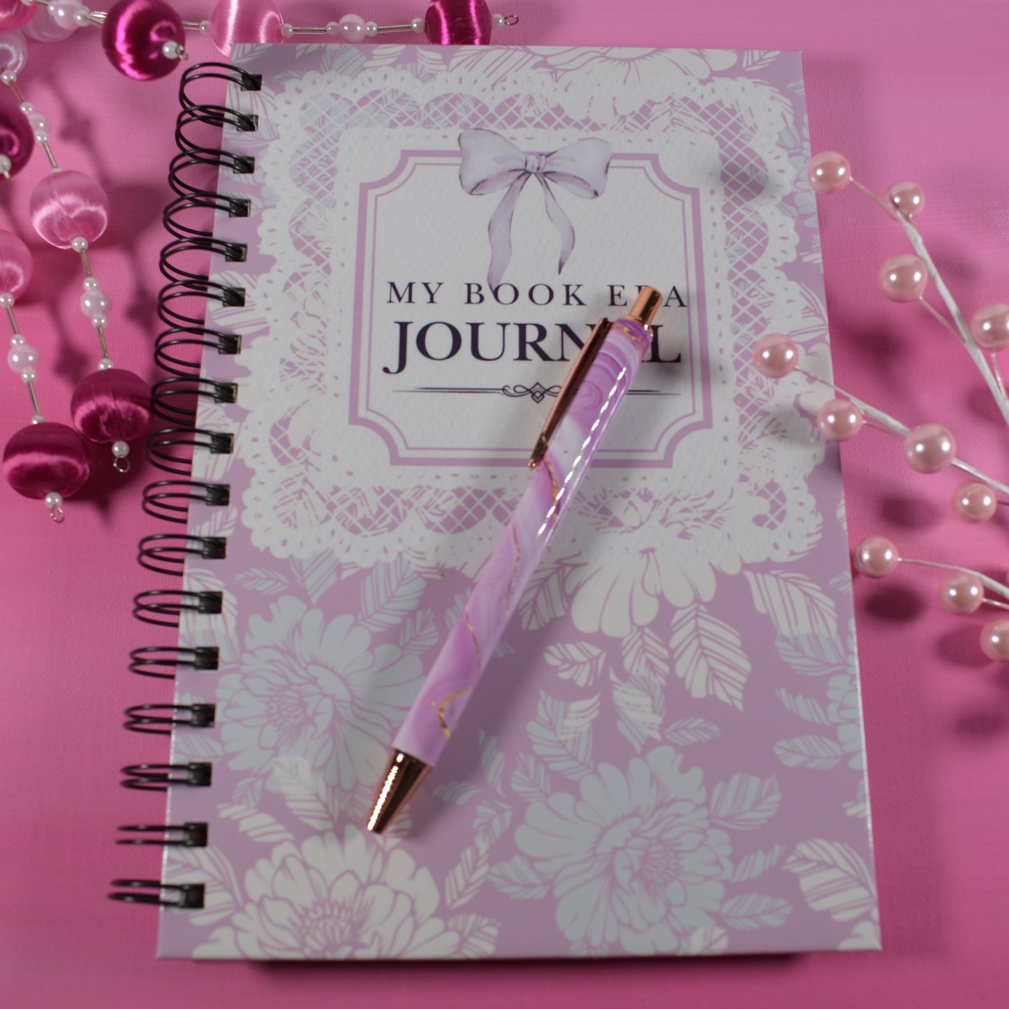 Pink journal with a pen on a pink background
