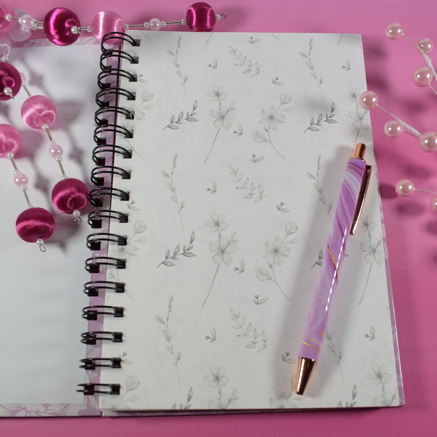 Notebook with a pink pen and decorative beads on a pink background