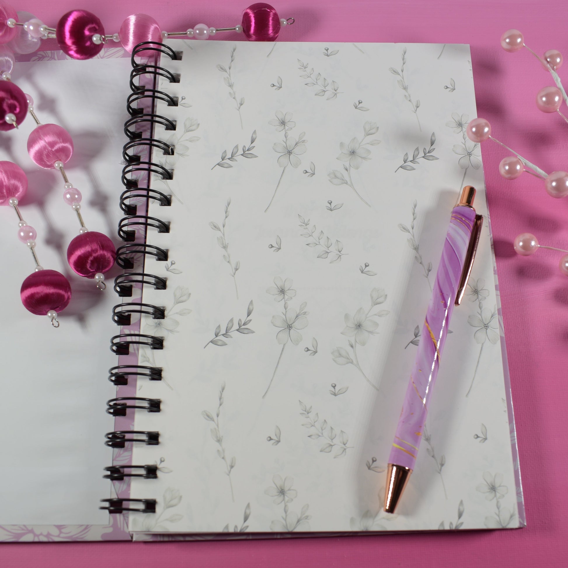 Notebook with a pink pen and decorative beads on a pink background