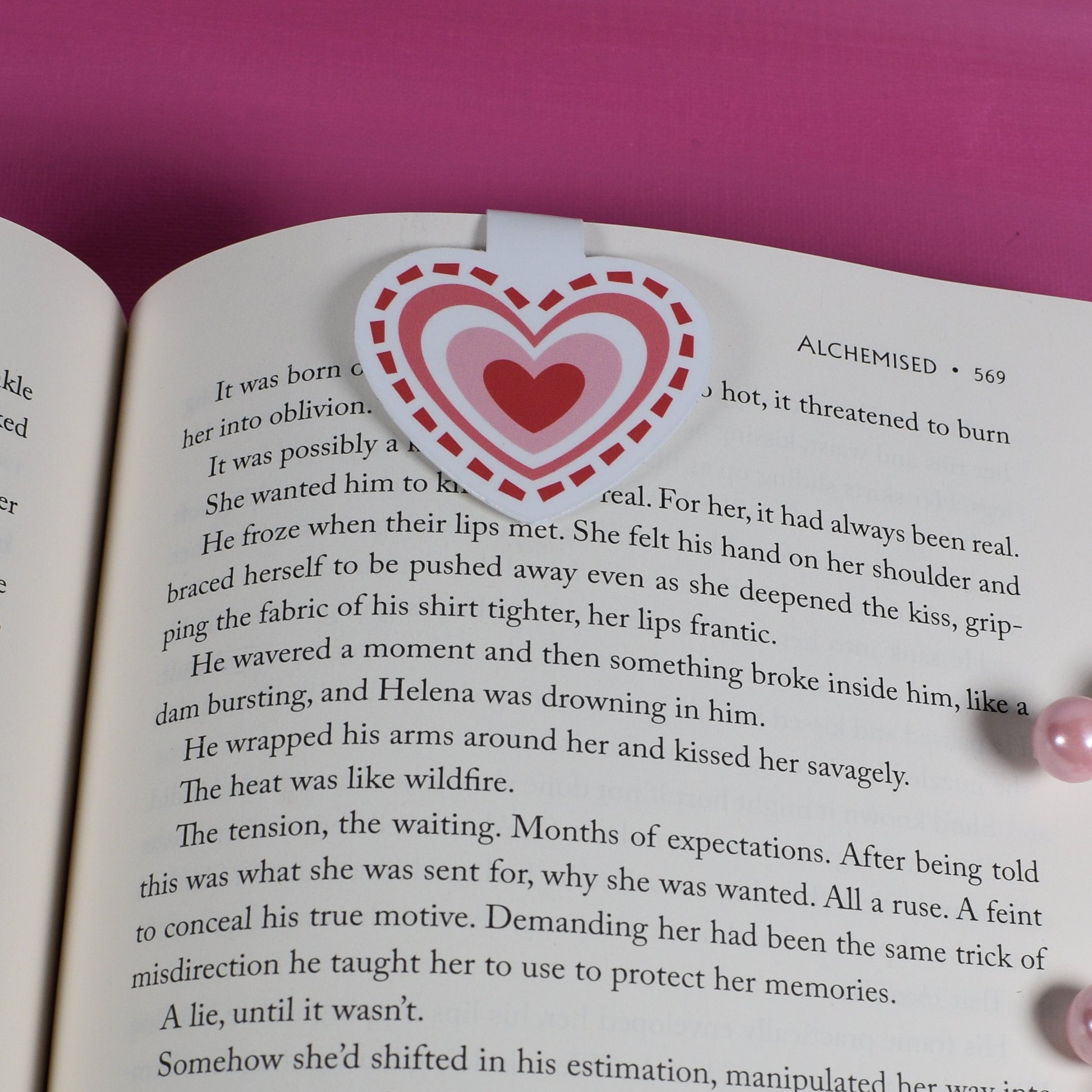 Open book with a heart bookmark on a pink background