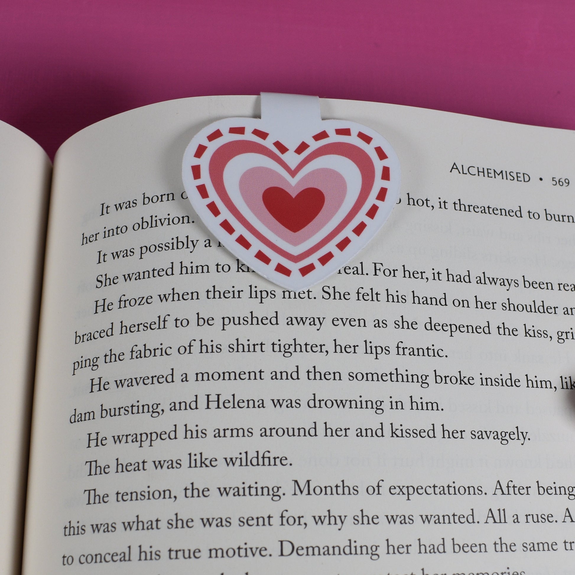 Open book with a heart-shaped sticker on a pink background