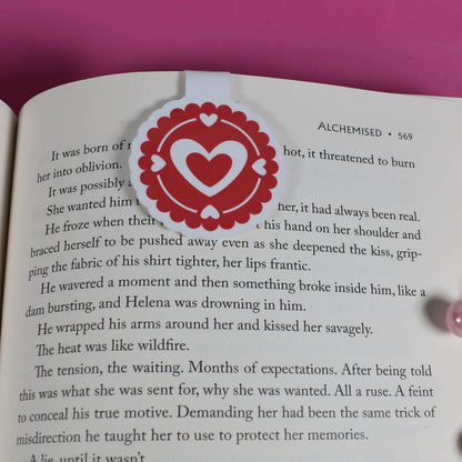 Open book with a heart-themed bookmark on a pink background