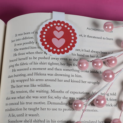 Open book with a decorative heart bookmark and pink beads on a pink background