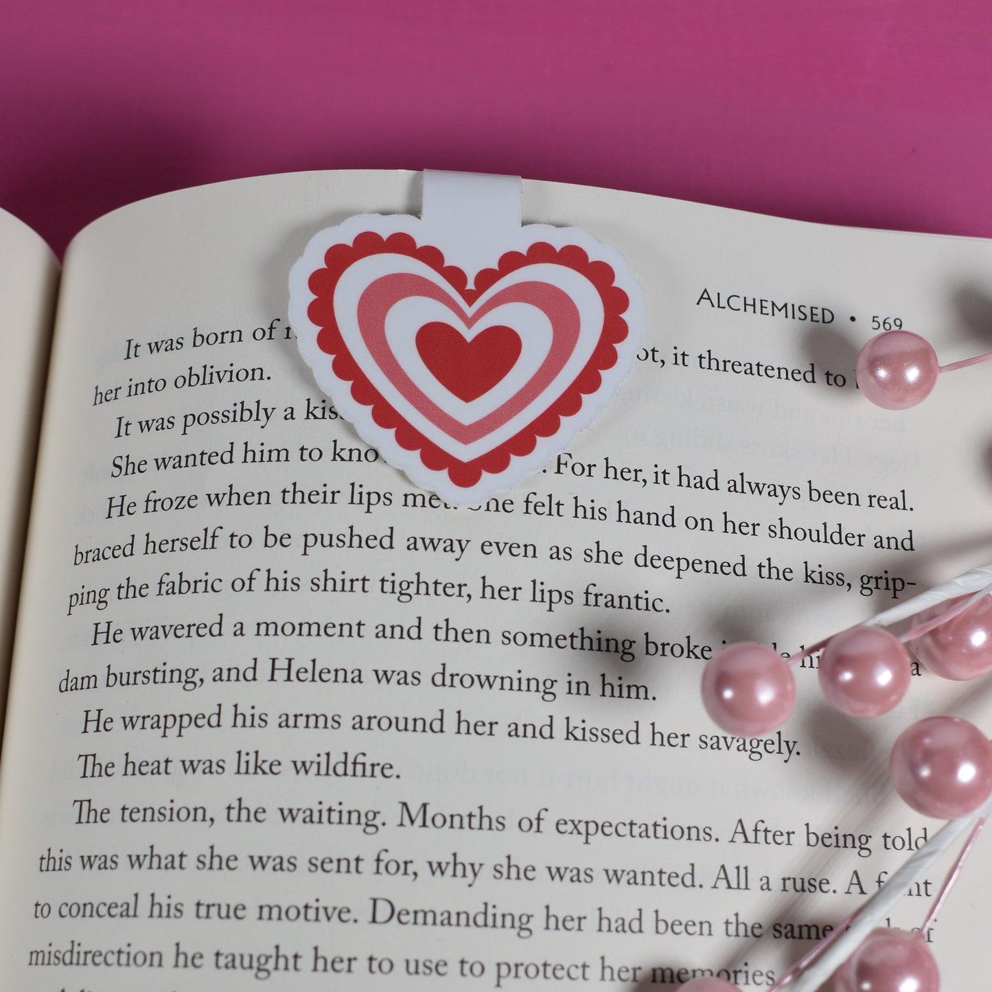 Open book with a heart-shaped bookmark on a pink background