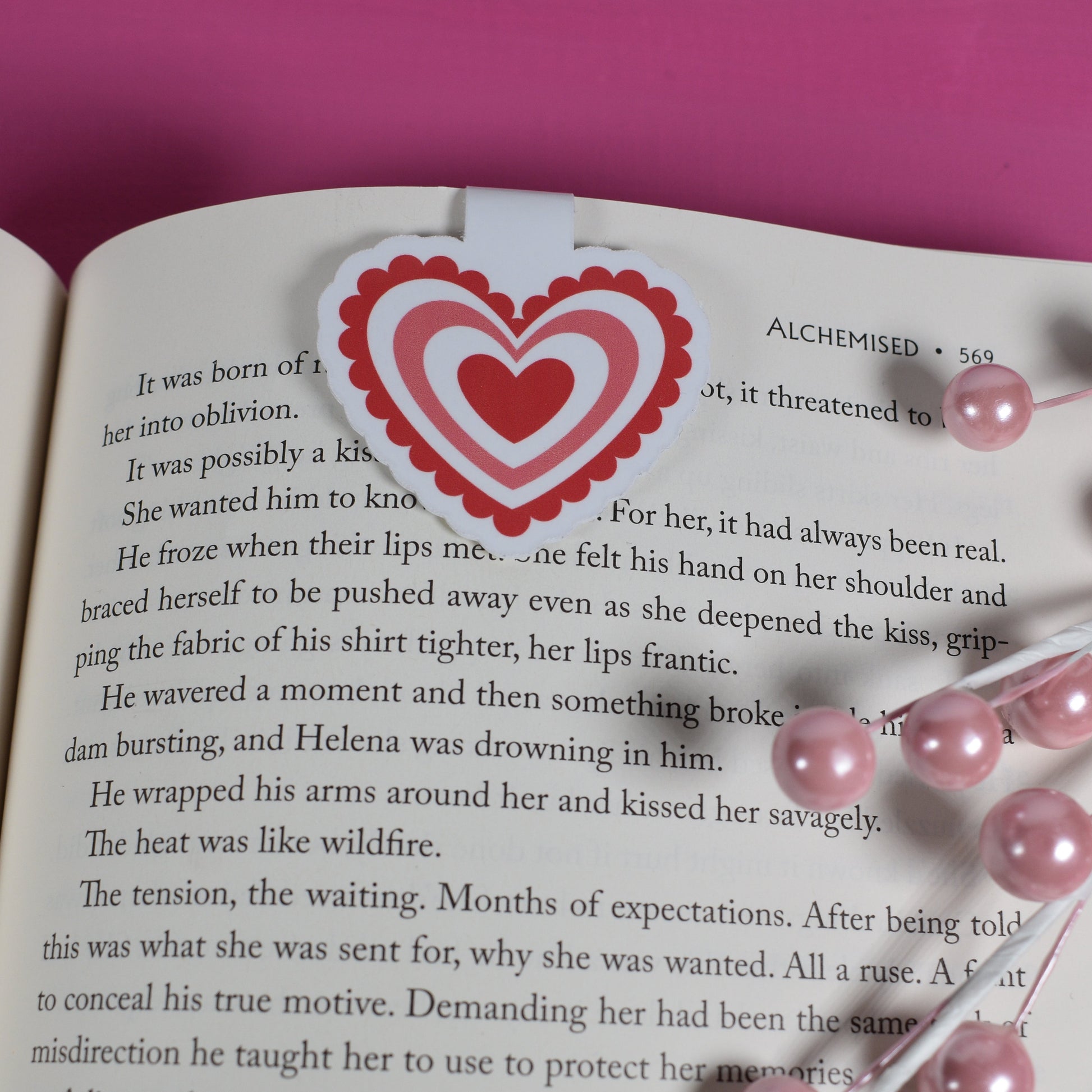 Open book with a heart-shaped bookmark on a pink background