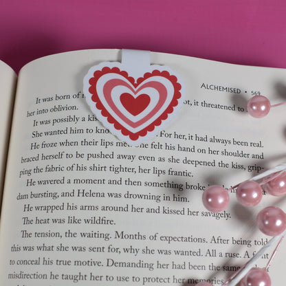 Open book with a heart-shaped bookmark on a pink background