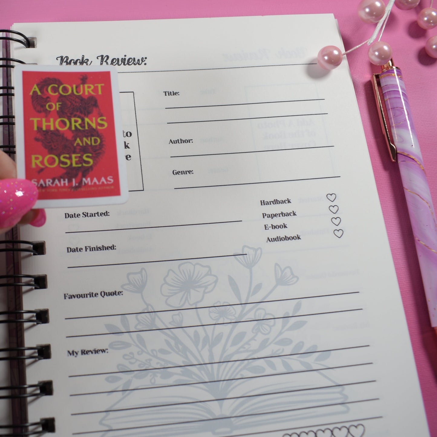 Hand holding a book with a bookmark featuring 'A Court of Thorns and Roses' on a pink background.