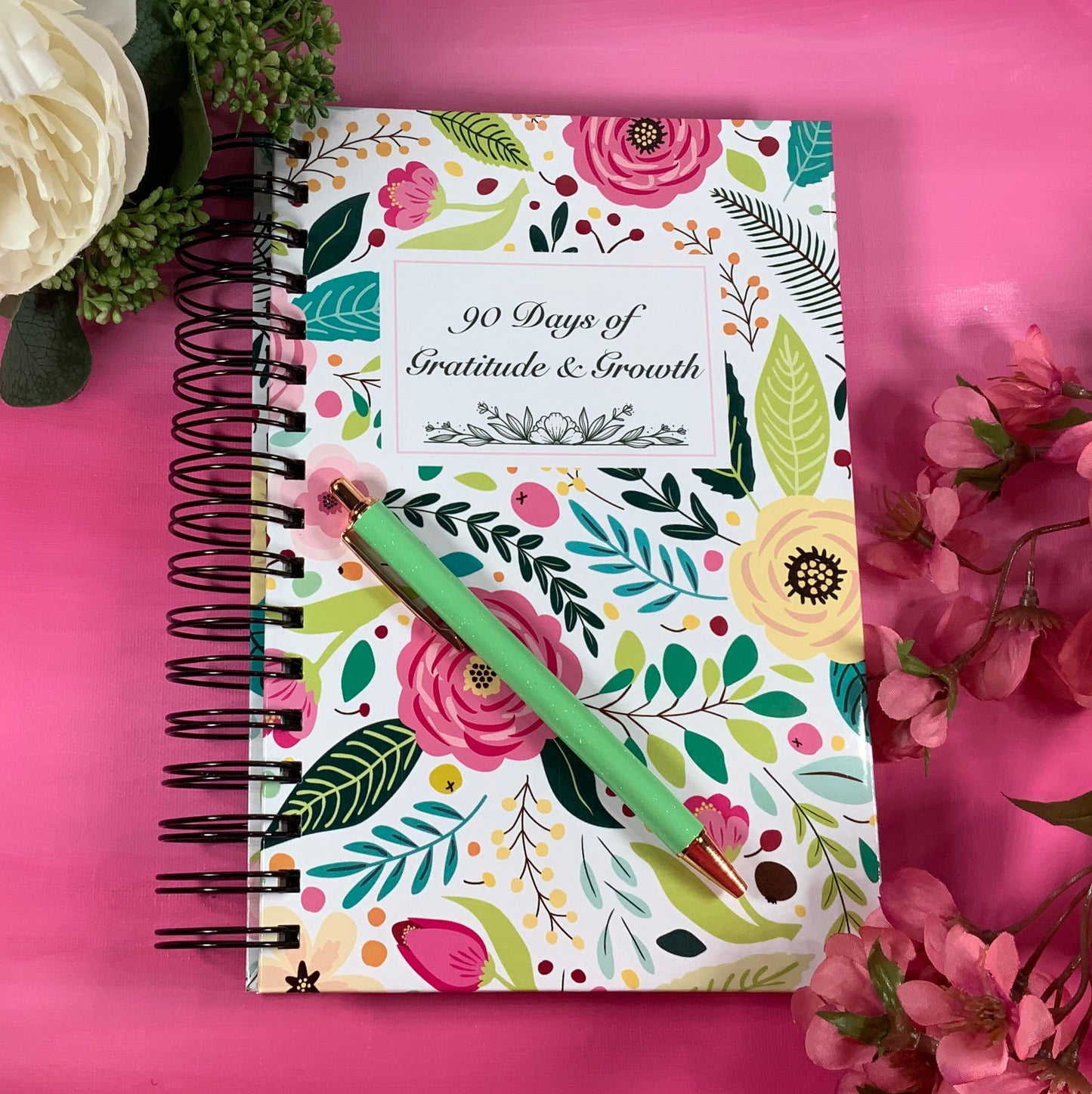 Notebook with floral design on a pink surface with flowers around