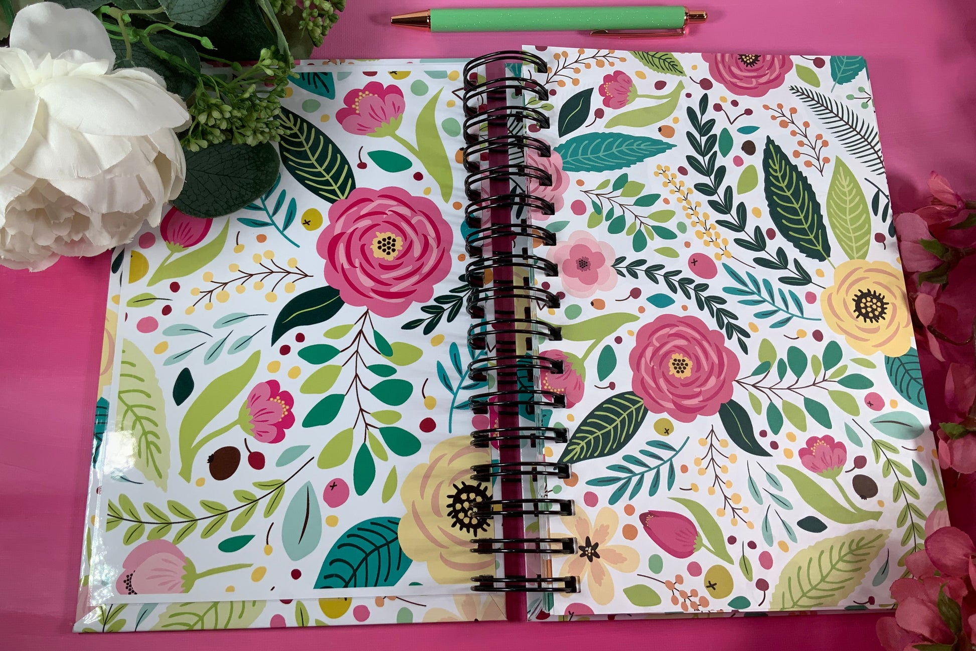 Floral-patterned notebook on a pink background with flowers and a pen.