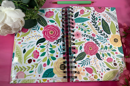 Floral-patterned notebook on a pink background with flowers and a pen.