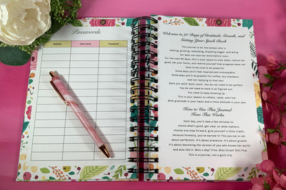Open planner with floral design on a pink background with flowers and a pen.
