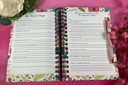 Open planner with printed pages on a pink background with flowers