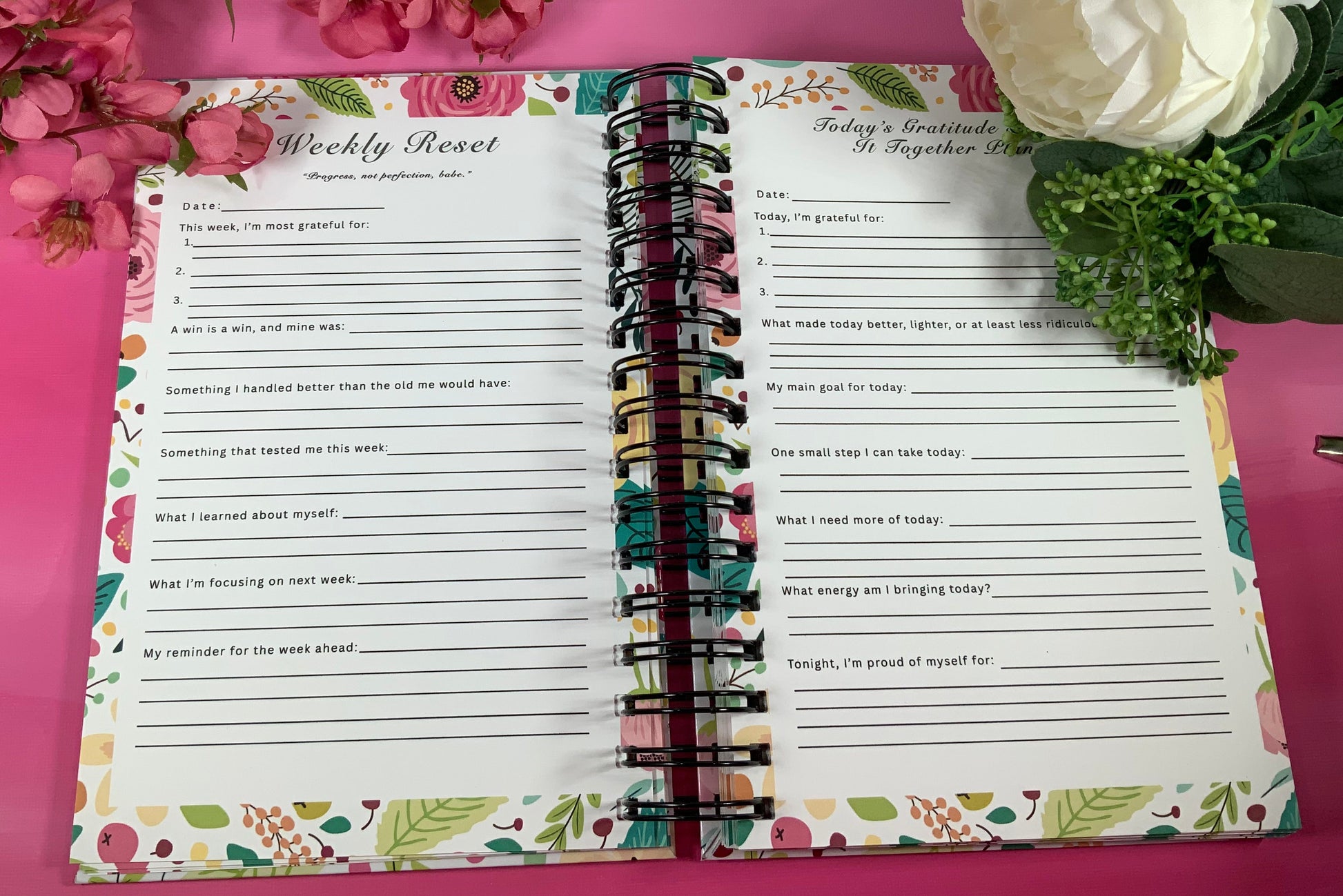 Open planner with weekly reset and reflection pages on a pink background with flowers.