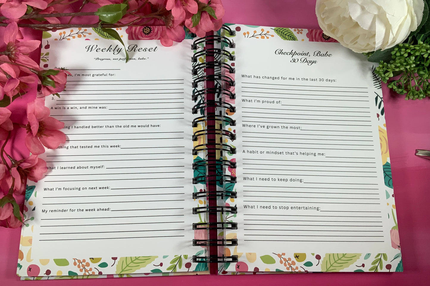 Open planner with weekly reset and gratitude lists on a pink surface with flowers.