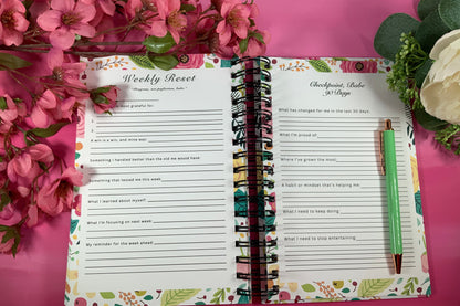Open planner with weekly反省页面 on a pink background with flowers