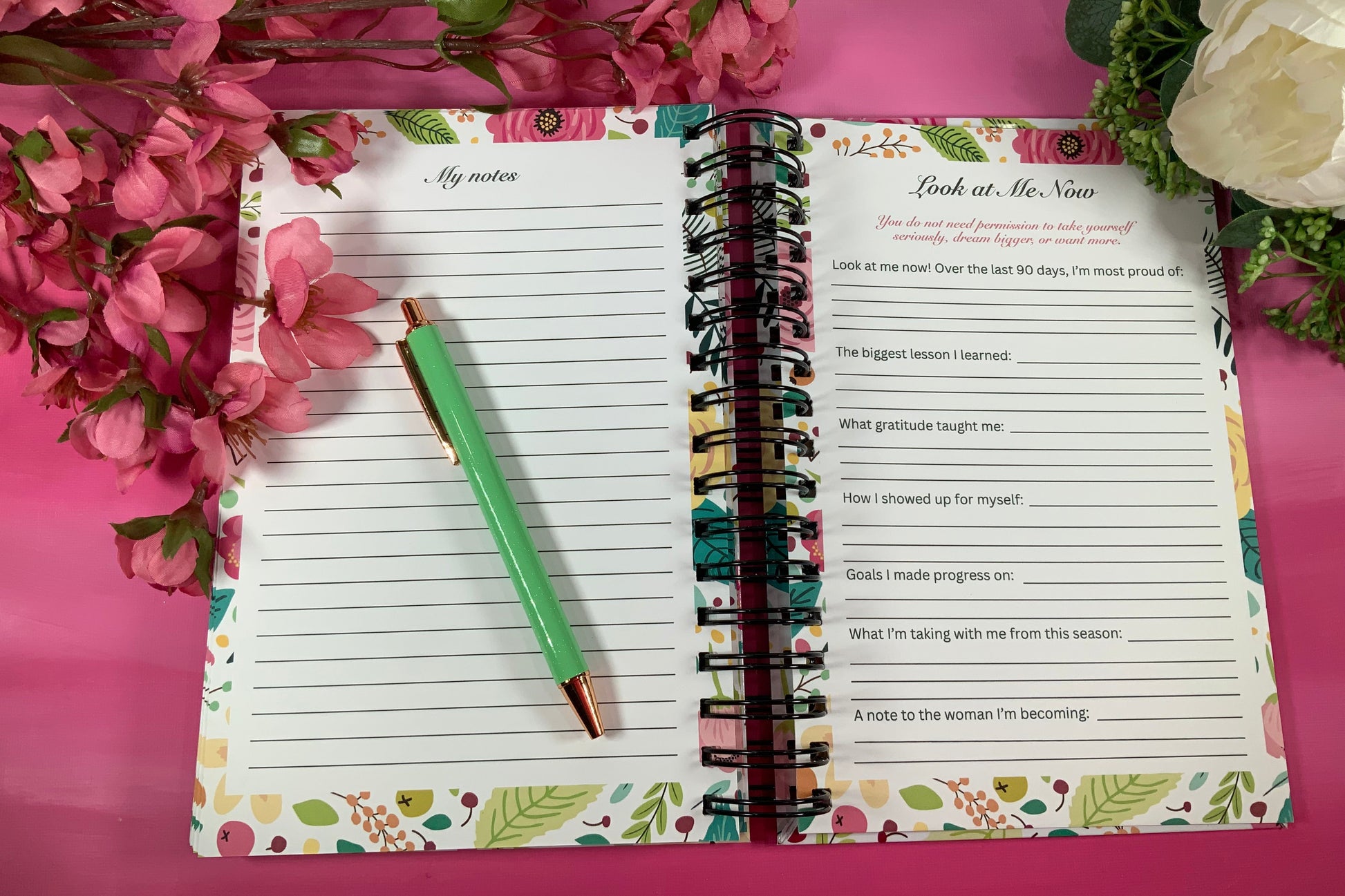 Open planner with floral design on a pink background with flowers and greenery.