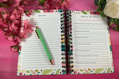 Open planner with floral design on a pink background with flowers and greenery.