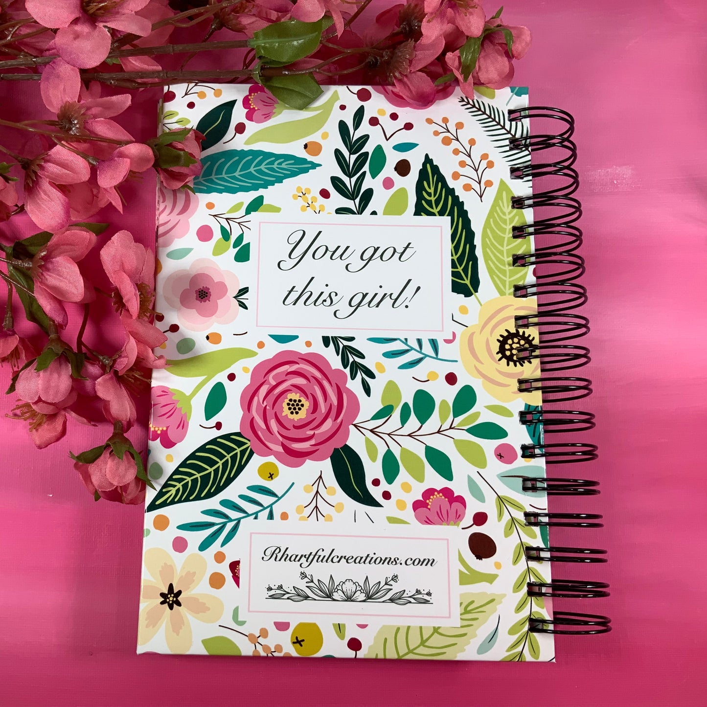 Notebook with floral design and motivational quote on a pink background