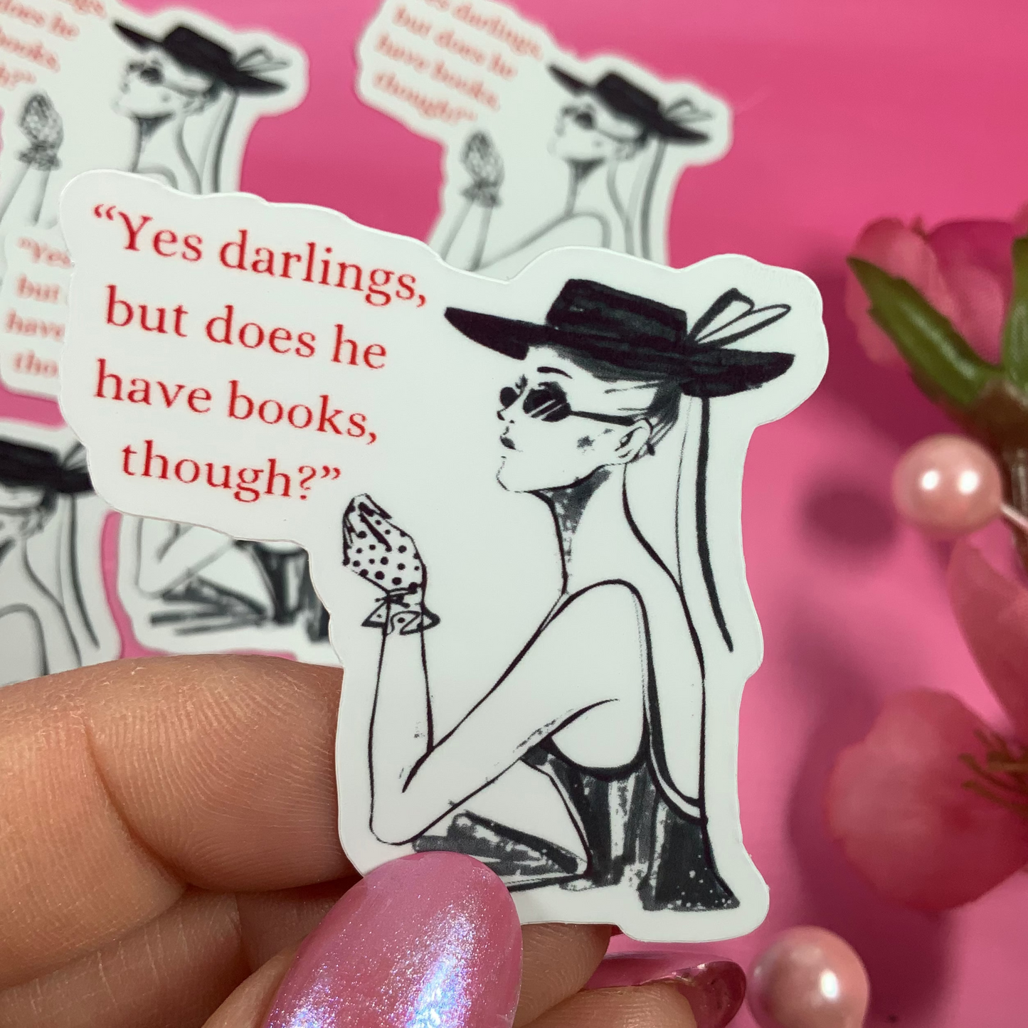 Sticker with a woman in a hat and text, held by a hand with pink nail polish against a pink background with flowers.