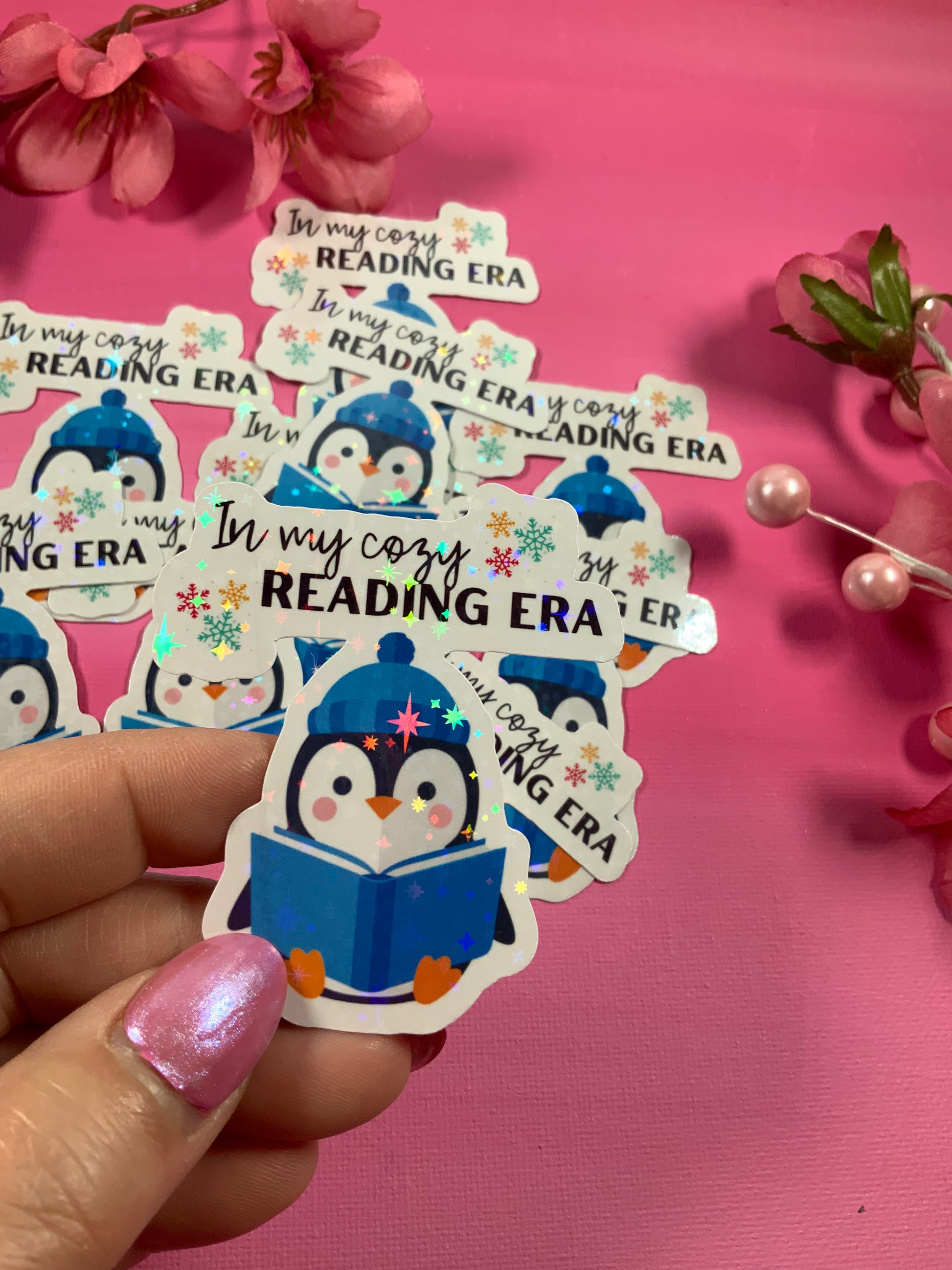 Sticker with a penguin reading a book and 'In my cozy READING ERA' text on a pink background.