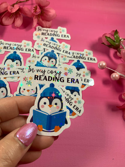 Sticker with a penguin reading a book and 'In my cozy READING ERA' text on a pink background.