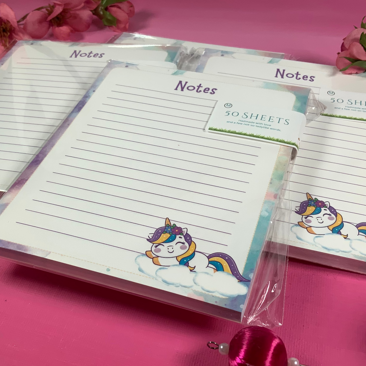 Notebook with unicorn design on a pink surface with flowers and decorative items.