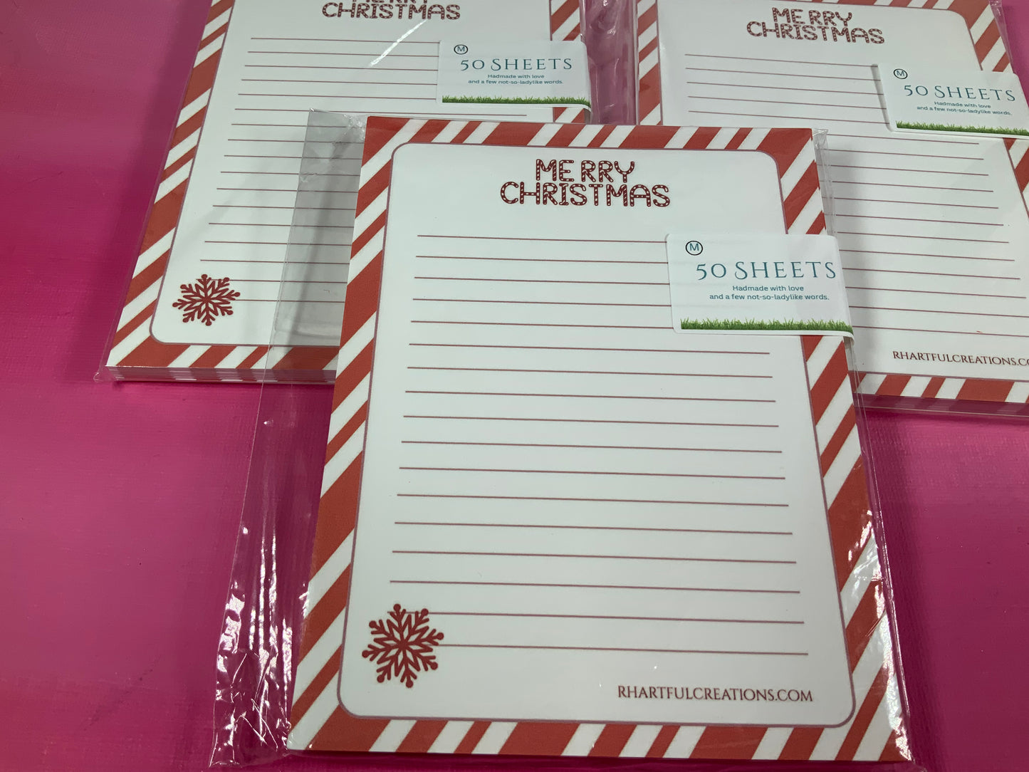 Set of Christmas-themed notepads with red and white striped borders on a pink background.