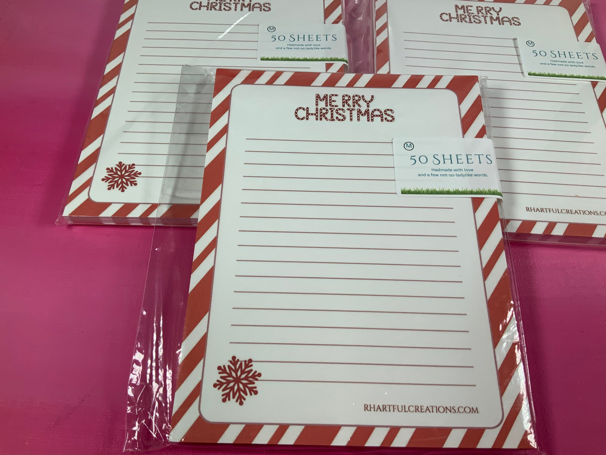 Set of Christmas-themed notepads with red and white striped borders on a pink background.