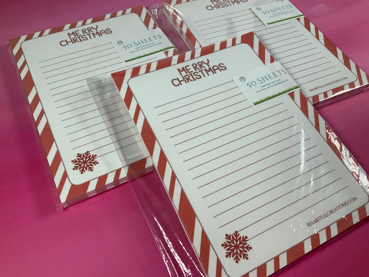 Merry Christmas-themed notepads with red and white striped borders on a pink background
