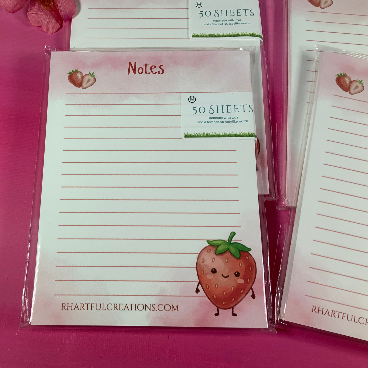 Notepads with strawberry design and 'Rhartful Creations' branding on a pink background