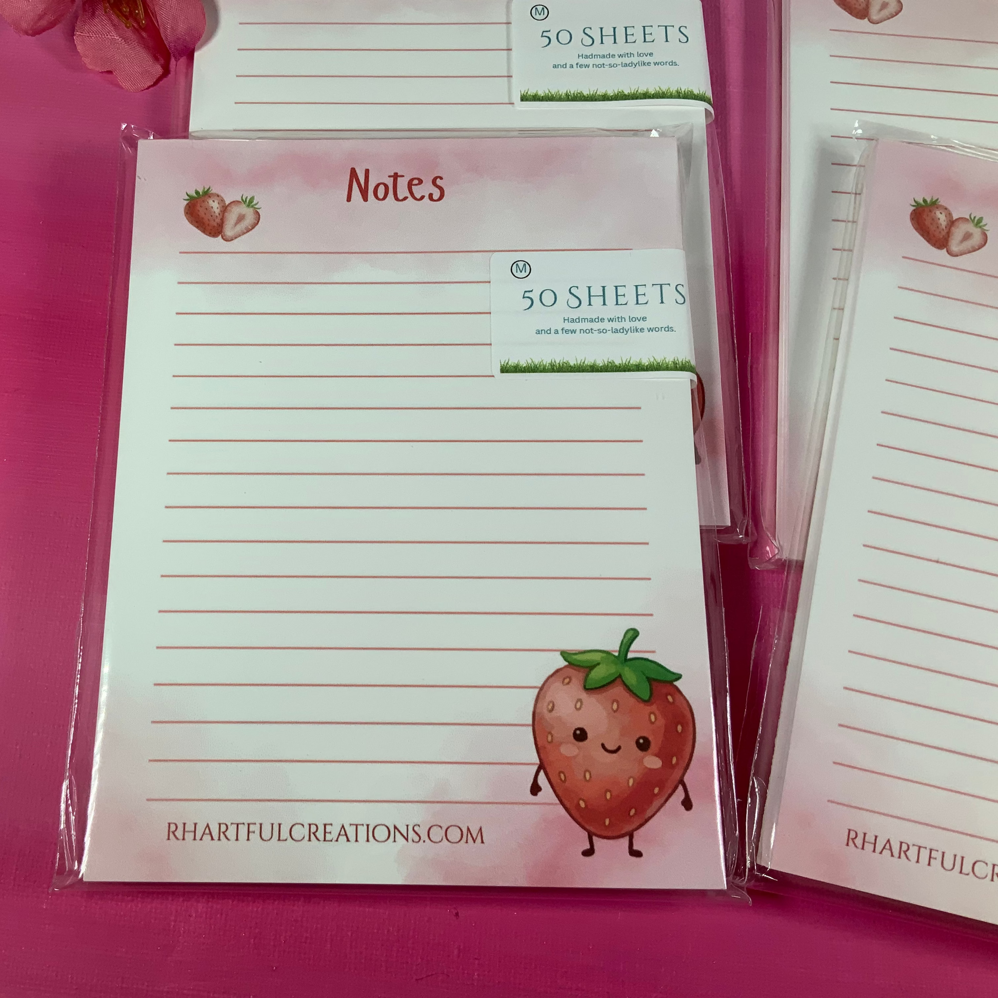 Notepads with strawberry design and 'Rhartful Creations' branding on a pink background