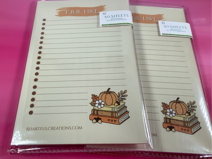 Two notepads with autumn-themed design on a pink background