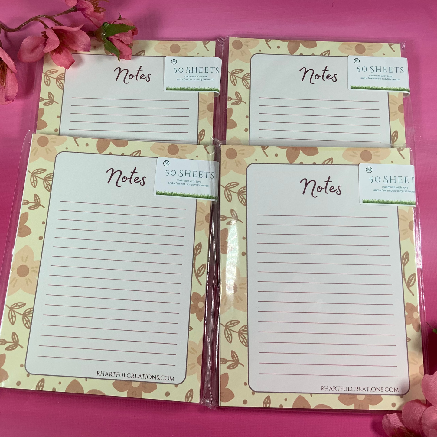Set of four floral note pads on a pink background with flowers.