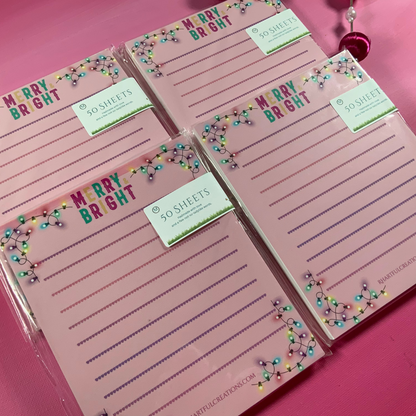 Set of pink notepads with 'Merry Bright' text and decorative elements on a pink background.