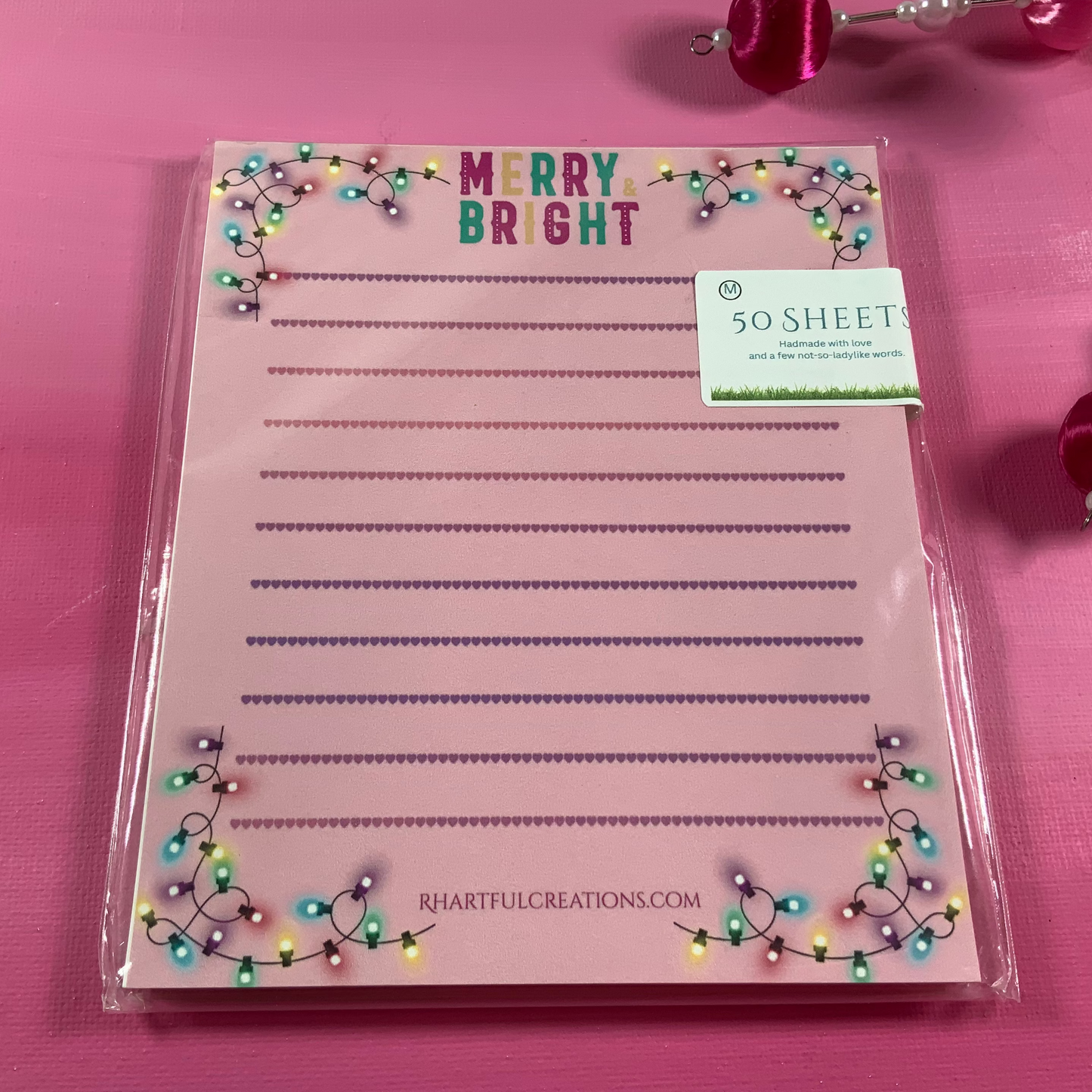 Pink notepad with 'Merry Bright' text and decorative lights on a pink background
