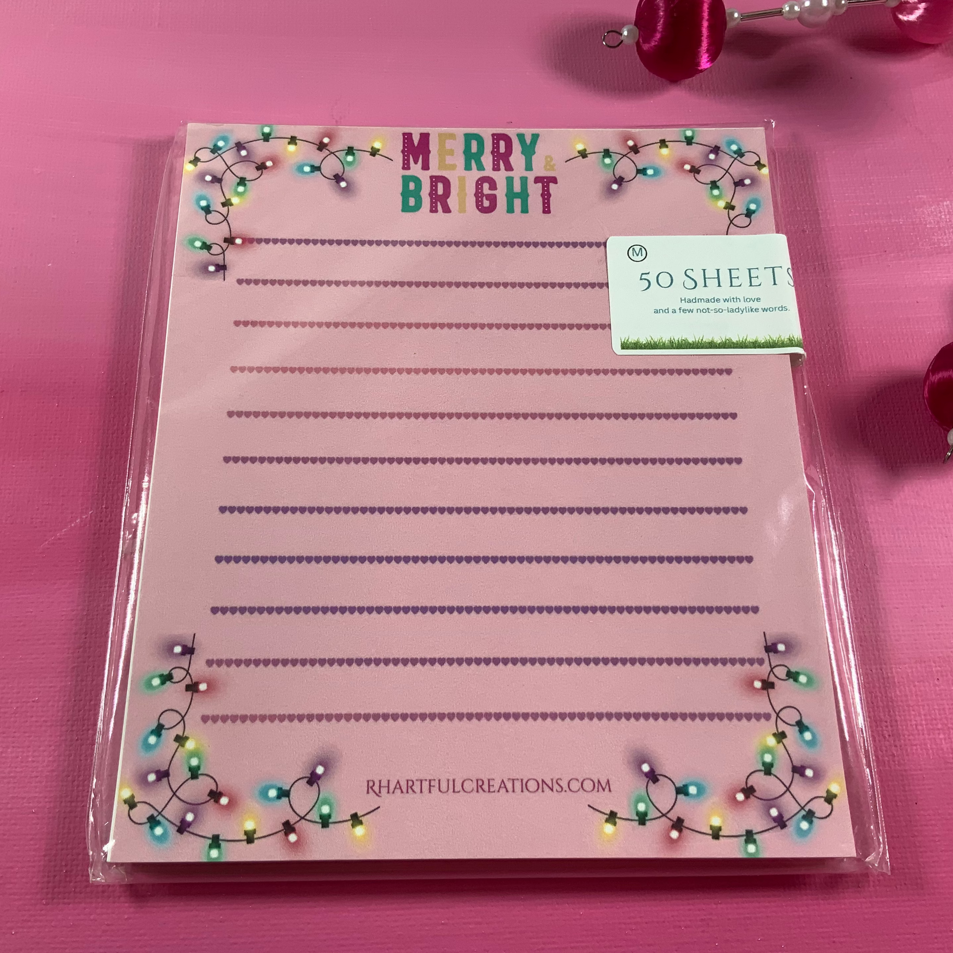 Pink notepad with 'Merry Bright' text and decorative lights on a pink background